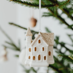 Image of white Christmas village house ornament with sparkly roof hanging from a Christmas tree.