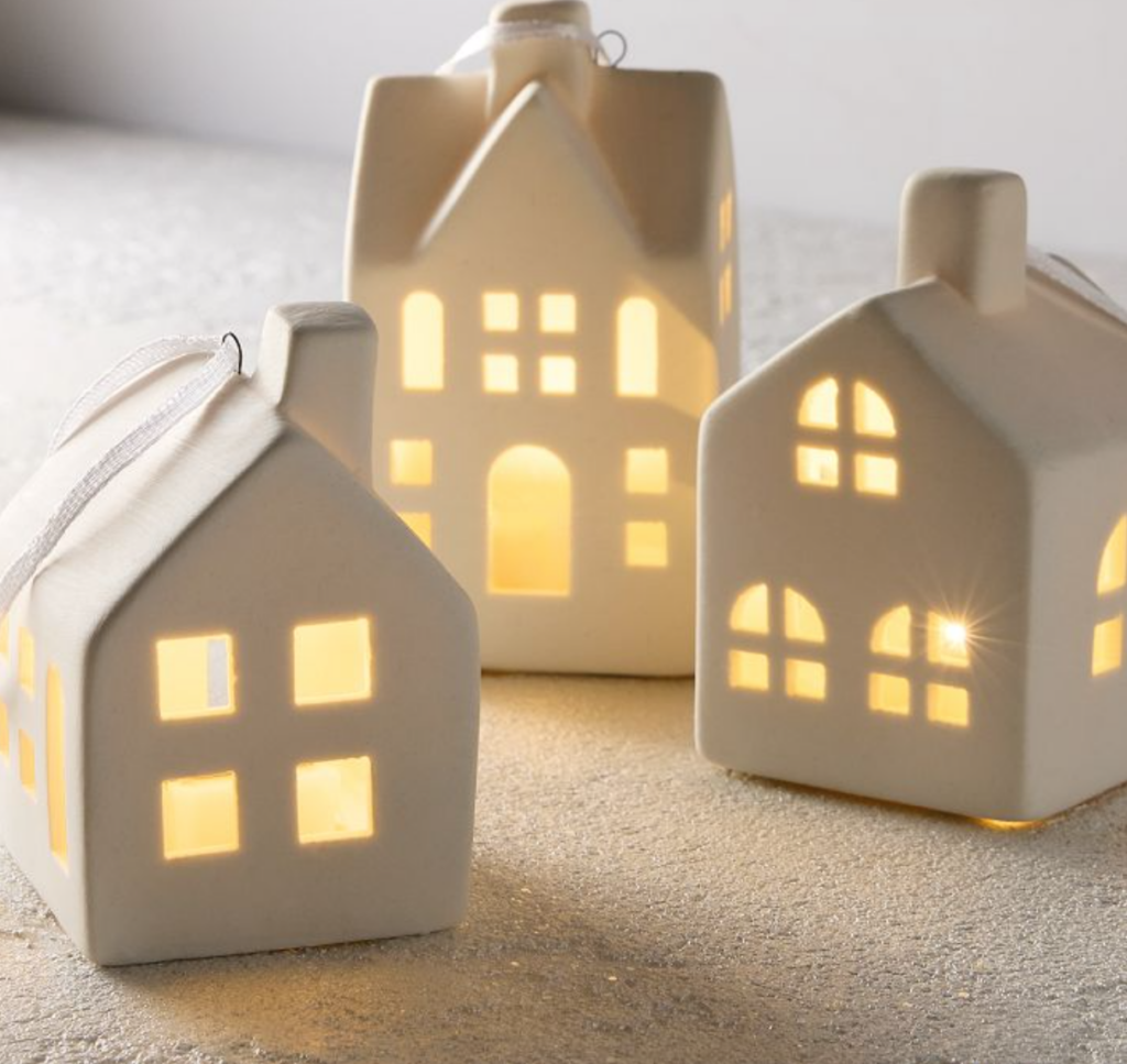 Image of 3 white Christmas village houses ornaments. Houses are two stories with chimneys and windows that are lit up.