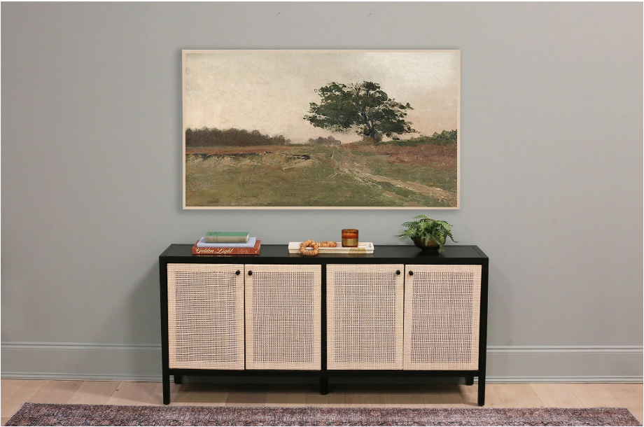 samsung frame tv art. Image of landscape of oak tree in front of green field on grey-green wall over black and tan credenza with red vintage rug in front.