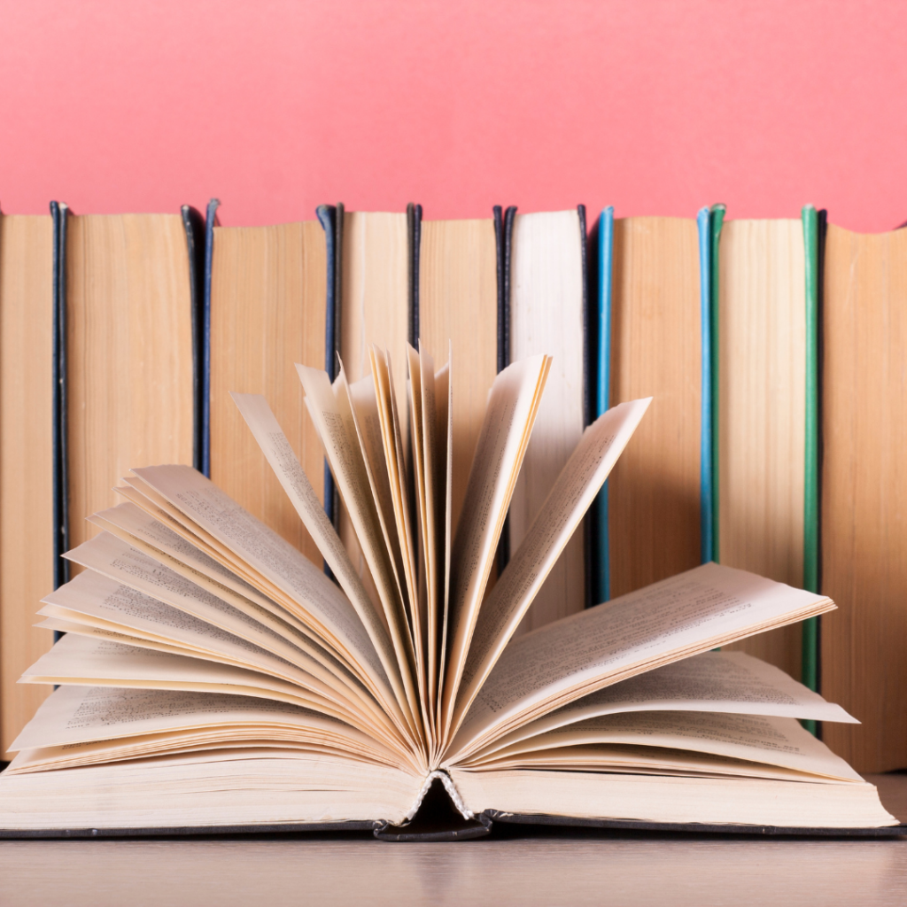 how to start a book club. Image of books lined up, pages facing out and one book open with pages fanned open. Background above the books is pink. 