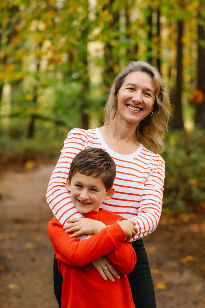 motherhood hacks products best advice Image of mother and son in forest smiling. Mother has blond hair and white and red striped long sleeve shirt and son is wearing a red shirt.
