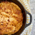 dutch oven lasagna. Picture of lasagna in cast iron dutch oven on grey quartz countertop with yellow and white striped cloth napkin.