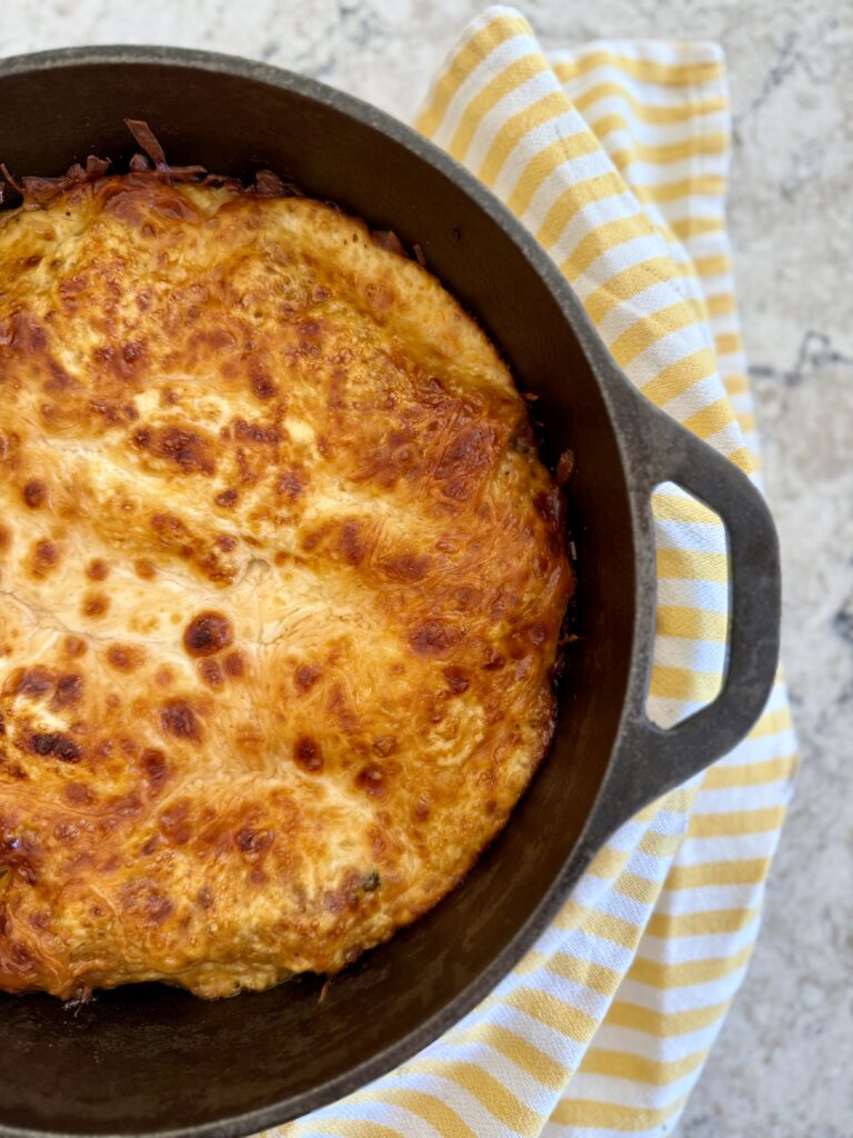 dutch oven lasagna. Picture of lasagna in cast iron dutch oven on grey quartz countertop with yellow and white striped cloth napkin.