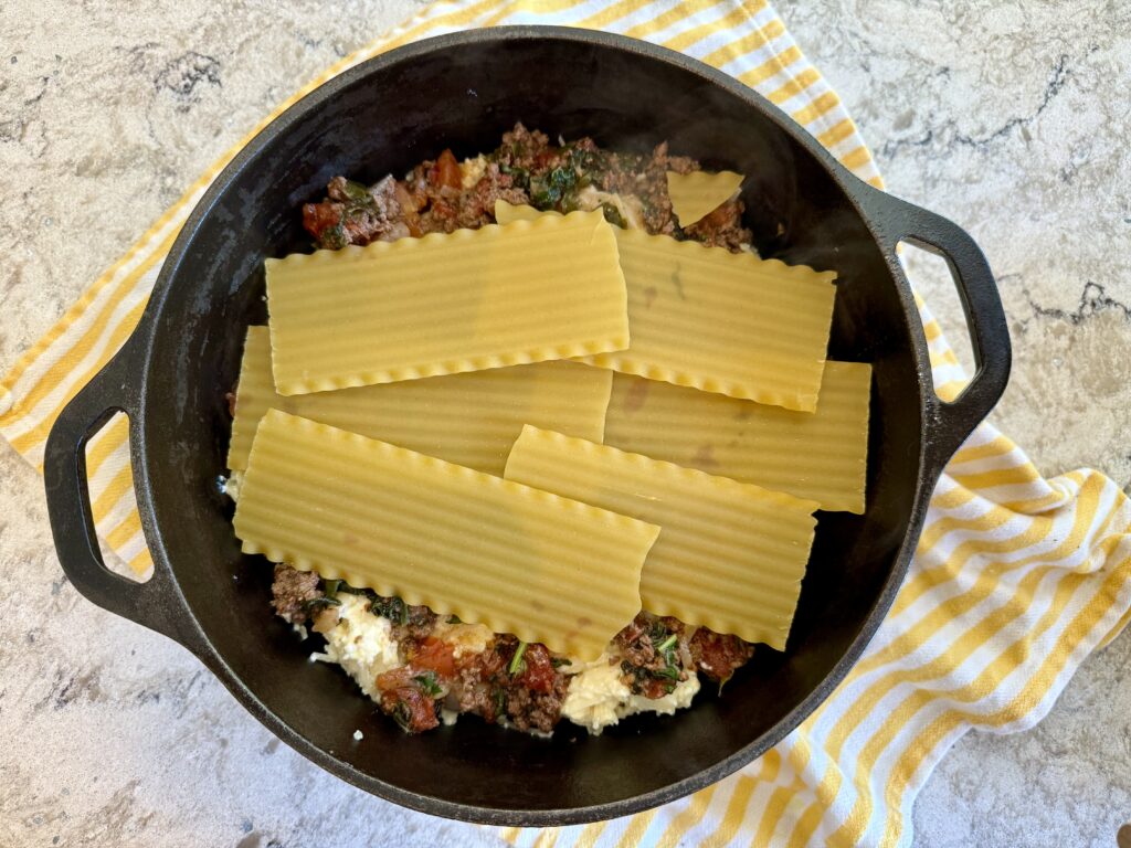 healthy dinner recipes. Image of  lasagna in dutch oven on a yellow and white striped towel on grey and white quartz countertop. 