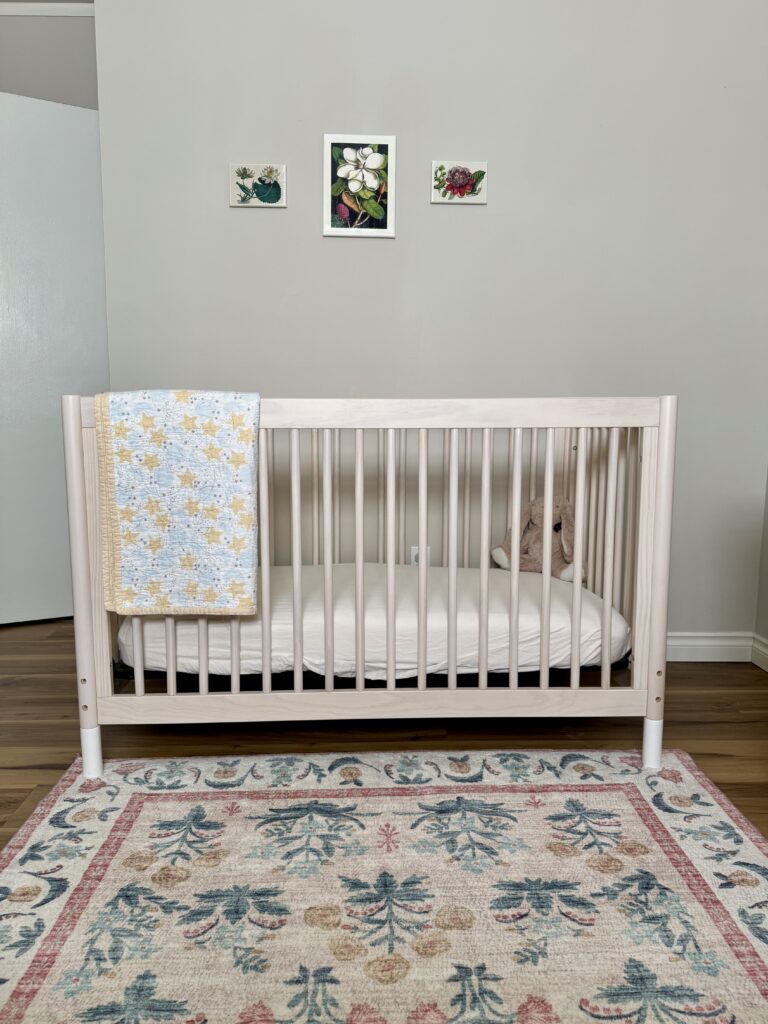 baby girl nursery decor ideas. Image of crib with quilt, vintage floral prints, and floral pattern rug. 