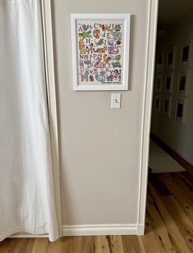 Image of framed cross stitch pattern - colorful alphabet with animals, hanging on a wall. 