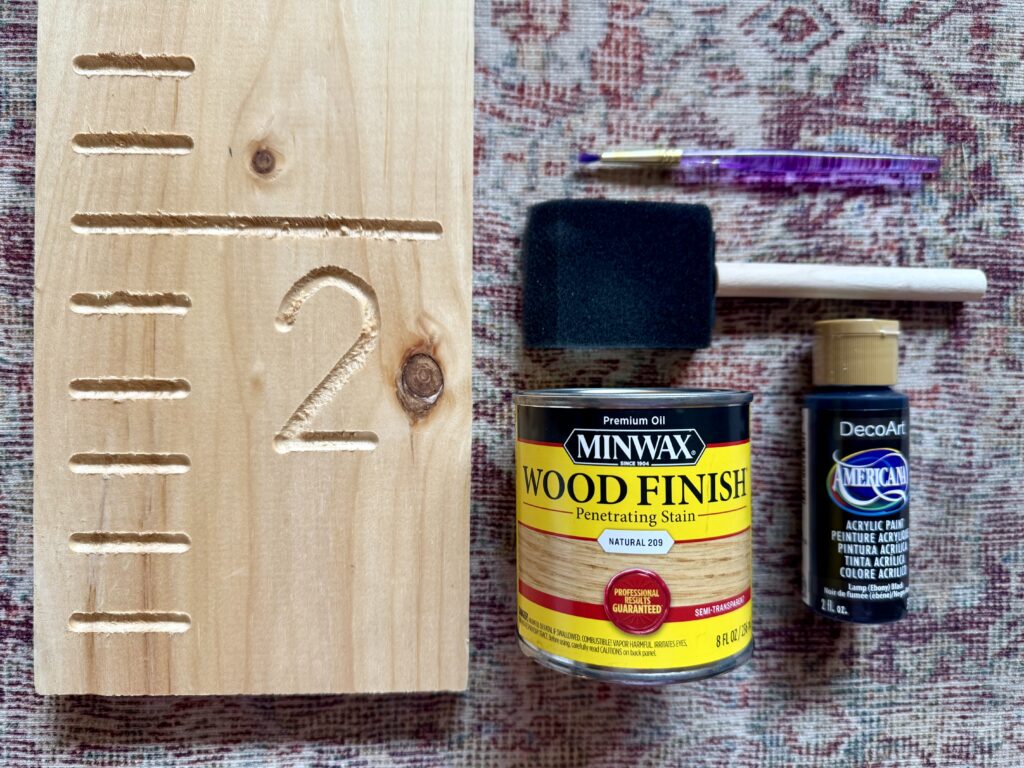wooden growth chart ruler. Image of supplies to make: wooden growth chart ruler, can of wood stain, foam paint brush, paint brush, and black acrylic paint.
