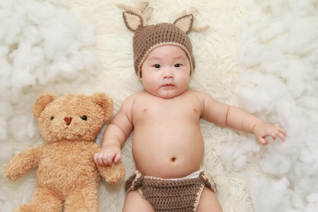 baby checklist new moms. Image of baby with knit hat and diaper next to teddy bear.