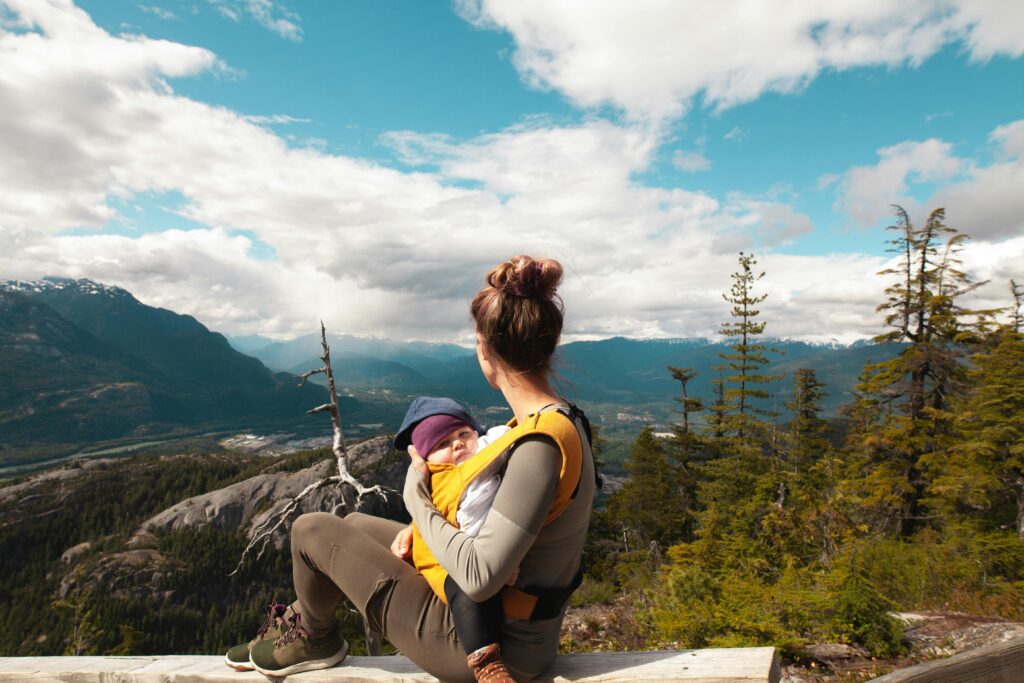 baby registry checklist. Image of woman on hike in the mountains with baby in yellow baby carrier.