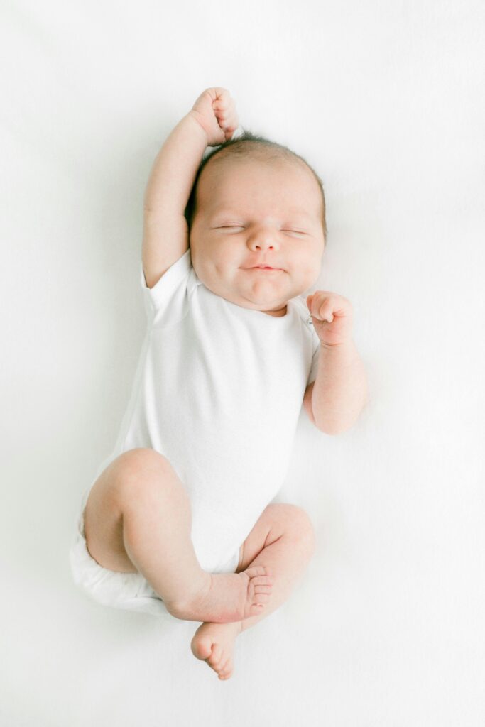 baby registry list. Image of newborn baby in white onesie stretching arm over head.