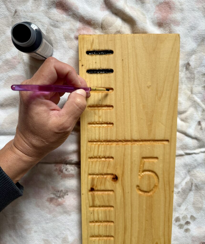 diy wooden growth chart ruler. Image of woman painting lines on a wooden growth chart ruler that's laying on a flower towel.