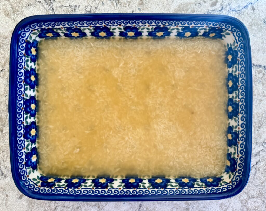 easy southwest chicken casserole recipe. Image of broth and rice in blue casserole dish on white quartz countertop.