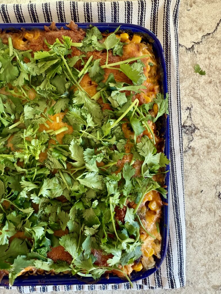 Image of Southwest Chicken Casserole, topped with cilantro in a blue baking dish and sitting on a striped dish towel on a grey and white quartz countertop. 