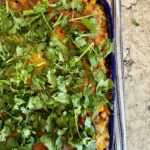 Image of Southwest Chicken Casserole, topped with cilantro in a blue baking dish and sitting on a striped dish towel on a grey and white quartz countertop.
