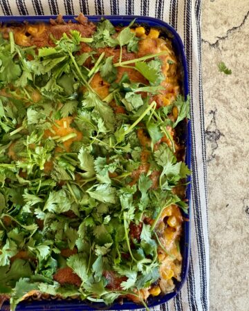 Image of Southwest Chicken Casserole, topped with cilantro in a blue baking dish and sitting on a striped dish towel on a grey and white quartz countertop.