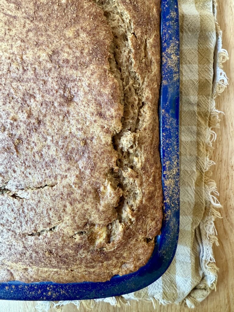 image of sourdough banana bread in blue loaf pan on tan and gingham cloth napkin.
