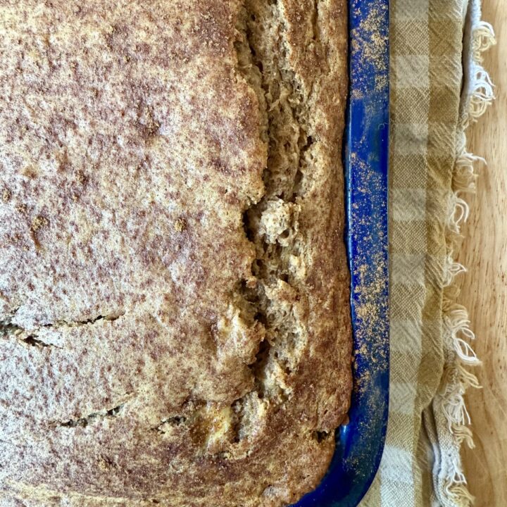 image of sourdough banana bread in blue loaf pan on tan and gingham cloth napkin.