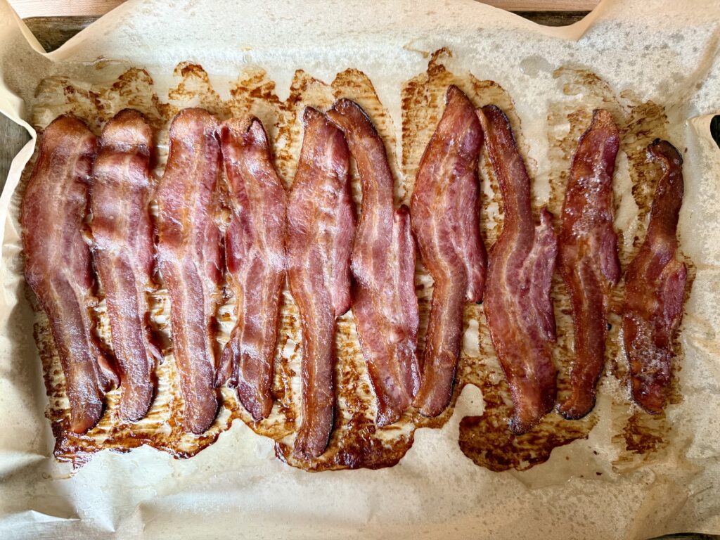 how to bake bacon in the oven. Image of cooked bacon on a sheet pan that is lined with parchment paper. 
