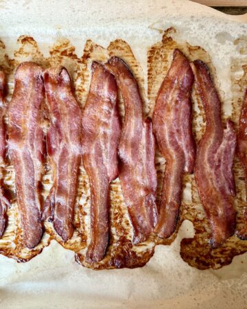 how to bake bacon in the oven. Image of cooked bacon on a sheet pan that is lined with parchment paper.