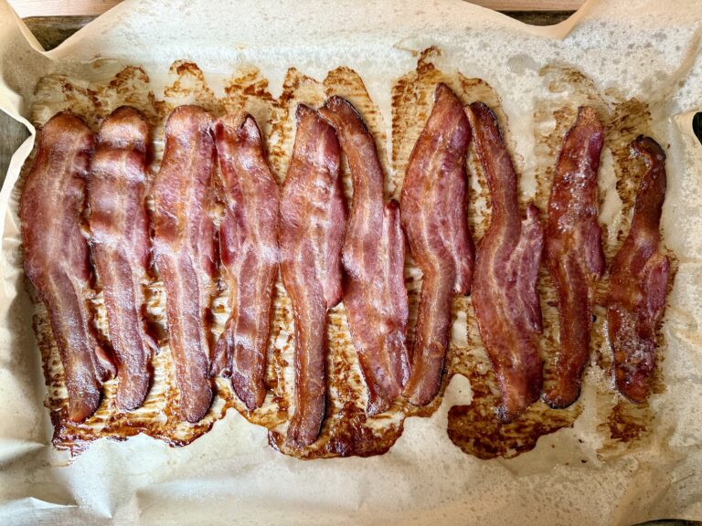how to bake bacon in the oven. Image of cooked bacon on a sheet pan that is lined with parchment paper.