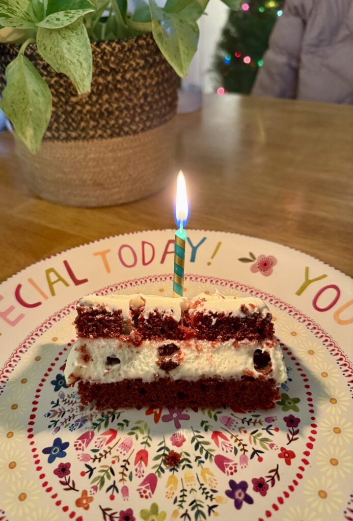birthday traditions. Image of slice of red velvet birthday cake with lit candle in it on You Are Special Today plate.