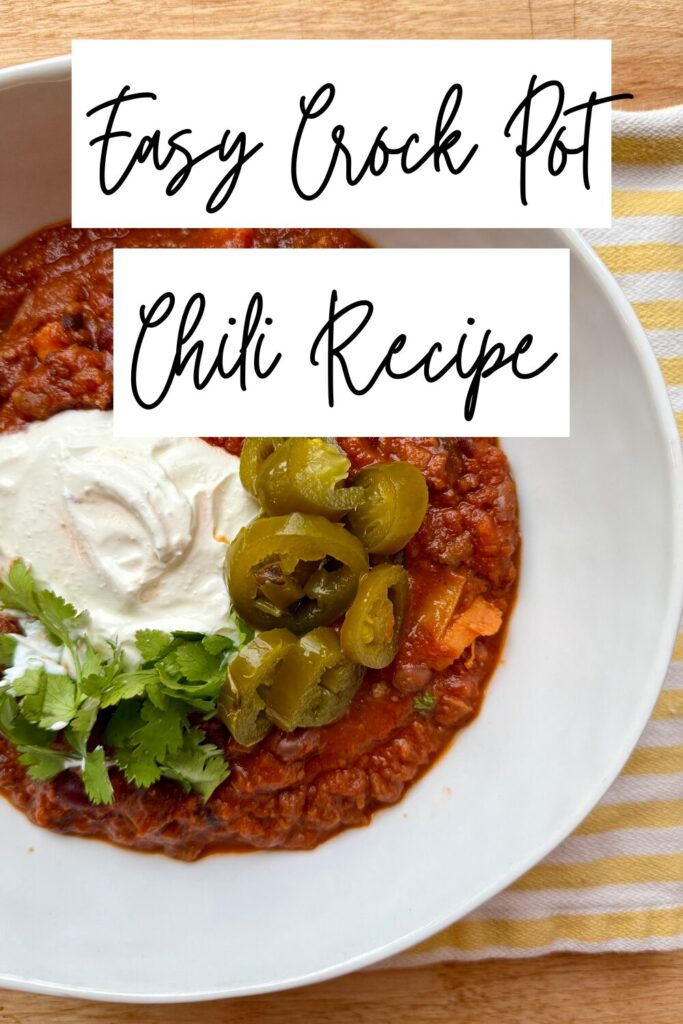 image of bowl of chili in white bowl on wooden counter with yellow and white striped napkin and text overlay that says "easy crock pot chili recipe"