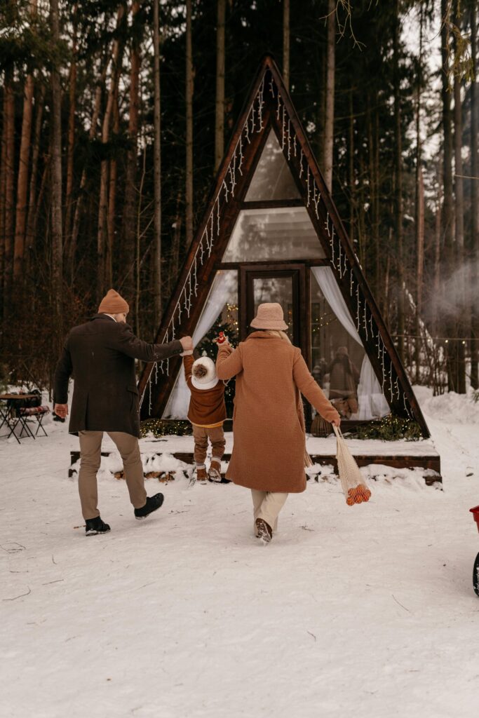 Image of man, woman, and child walking in snow to an A-frame cabin in the woods. 