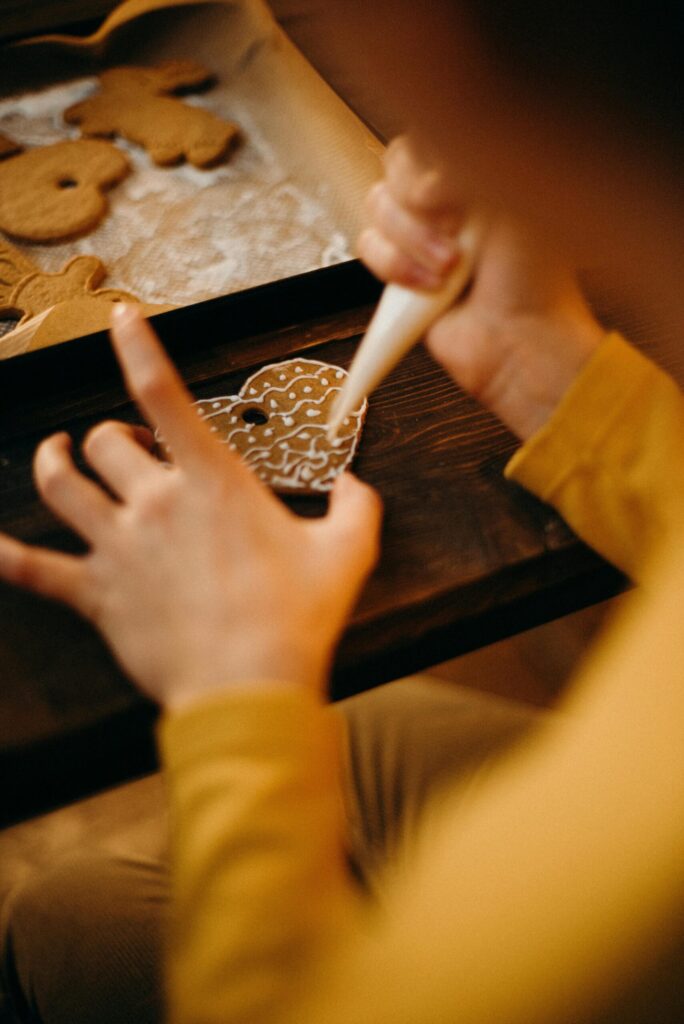 Christmas family traditions. Image of child decorating gingerbread cookies with white frosting. 