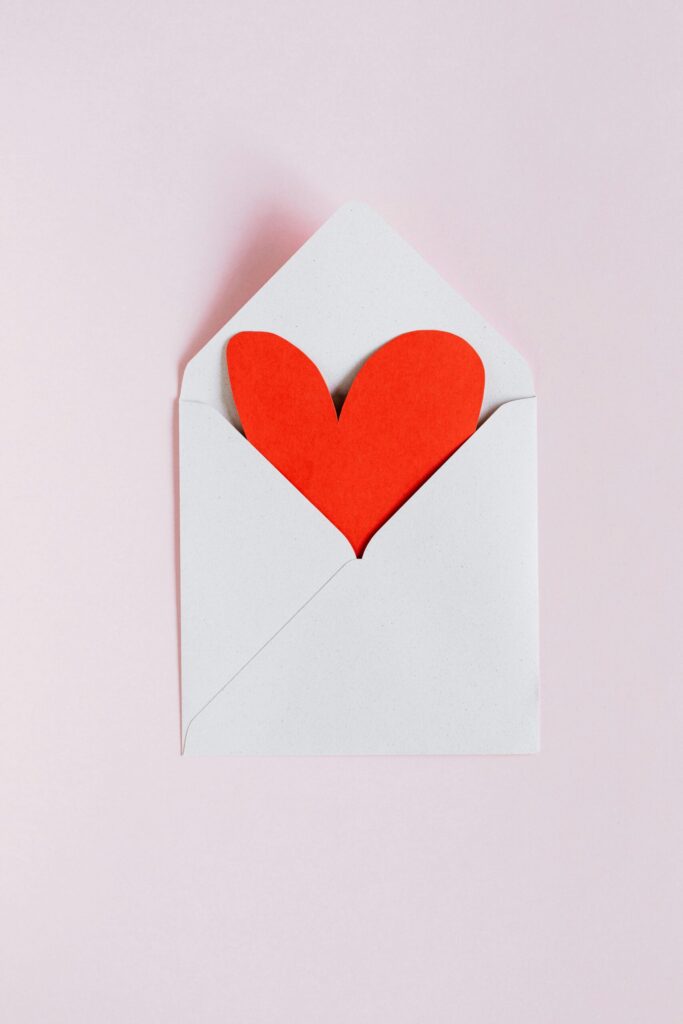 valentine's day gifts. Image of red paper heart in white envelop with pink background.