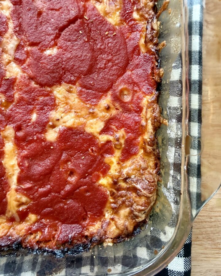 Image of chili relleno casserole recipe in glass pyrex dish on top of a black and white checkered cloth napkin on wooden countertop.