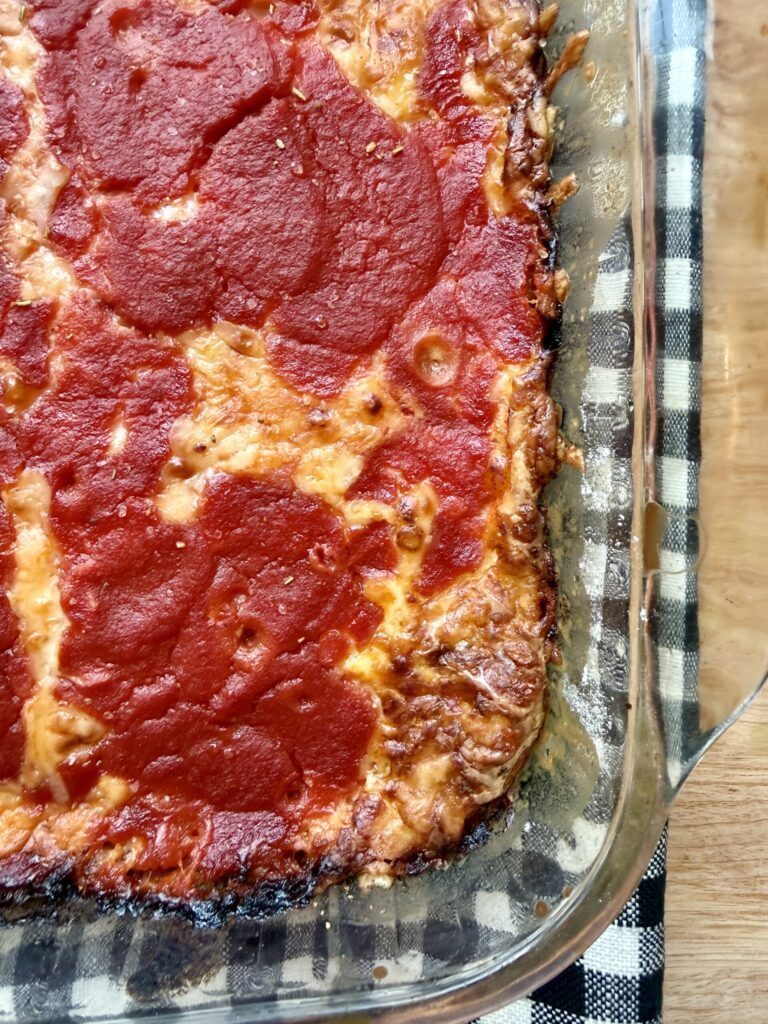 Image of chili relleno casserole recipe in glass pyrex dish on top of a black and white checkered cloth napkin on wooden countertop.