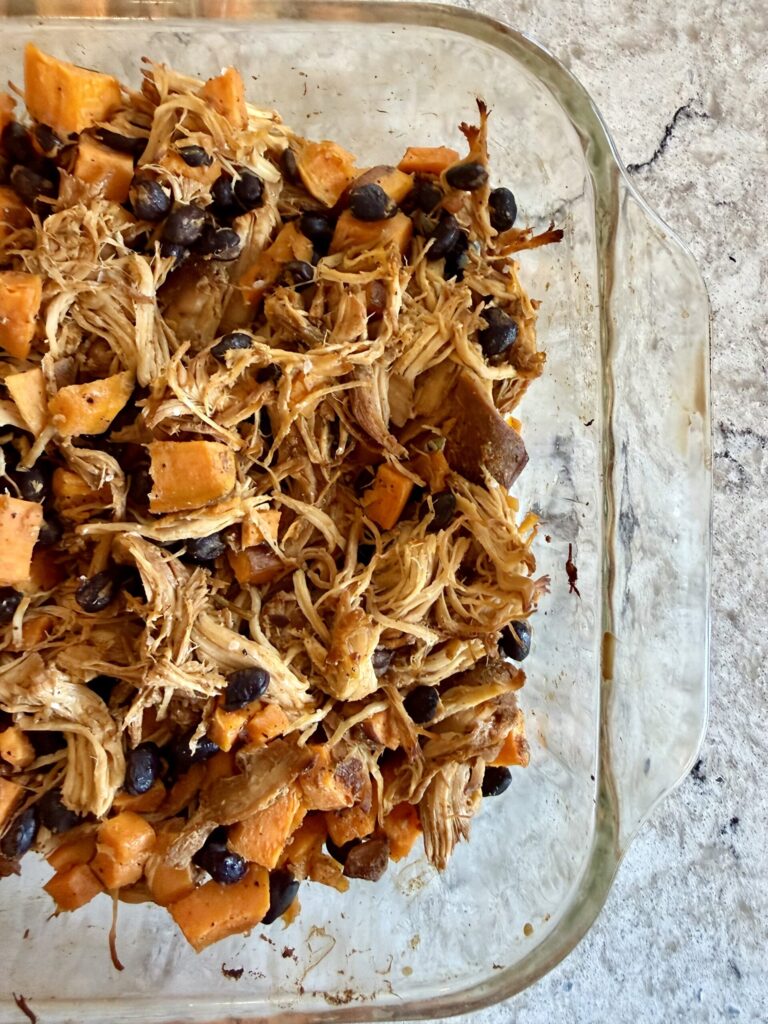 easy meal prep hacks. Image of shredded chicken, diced sweet potato, and black beans in glass casserole dish on grey, white and brown quartz countertop. 