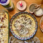 meal prep. Image of egg casserole, quiche, grated potato, pesto, salt and pepper, and a lit candle on a wooden table.
