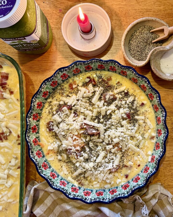 meal prep. Image of egg casserole, quiche, grated potato, pesto, salt and pepper, and a lit candle on a wooden table.