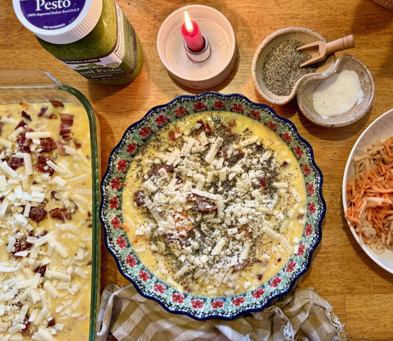 meal prep. Image of egg casserole, quiche, grated potato, pesto, salt and pepper, and a lit candle on a wooden table.