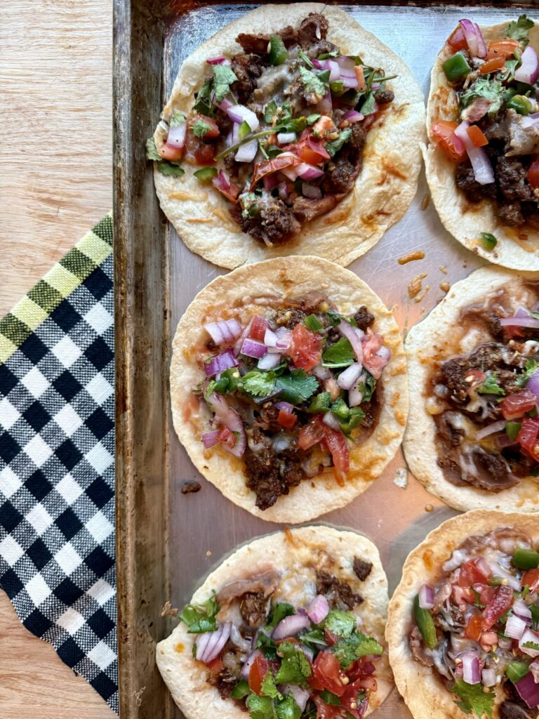 image of sheet pan tacos with ground beef and pico de gallo on sheet pan with black and white checkered dish towel.
