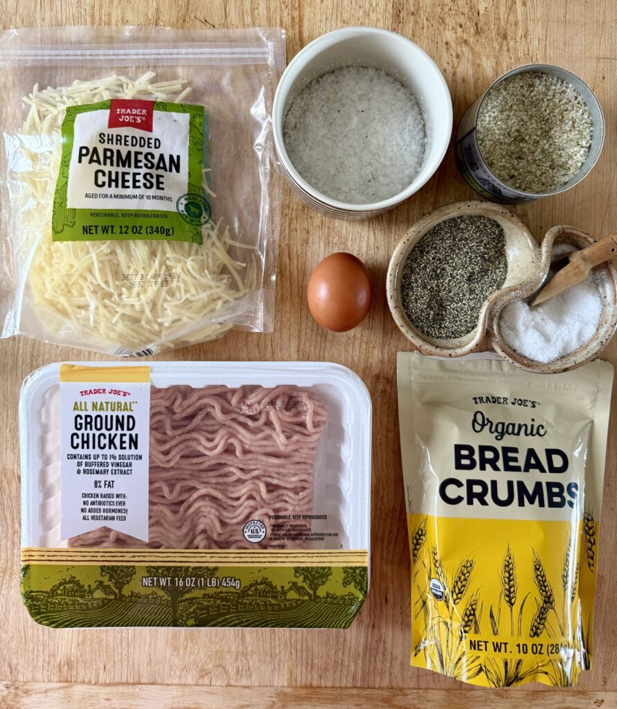 chicken parmesan meatballs ingredients: parmesan cheese, salt, seasoning, salt and pepper, ground chicken, bread crumbs on butcher block counter.