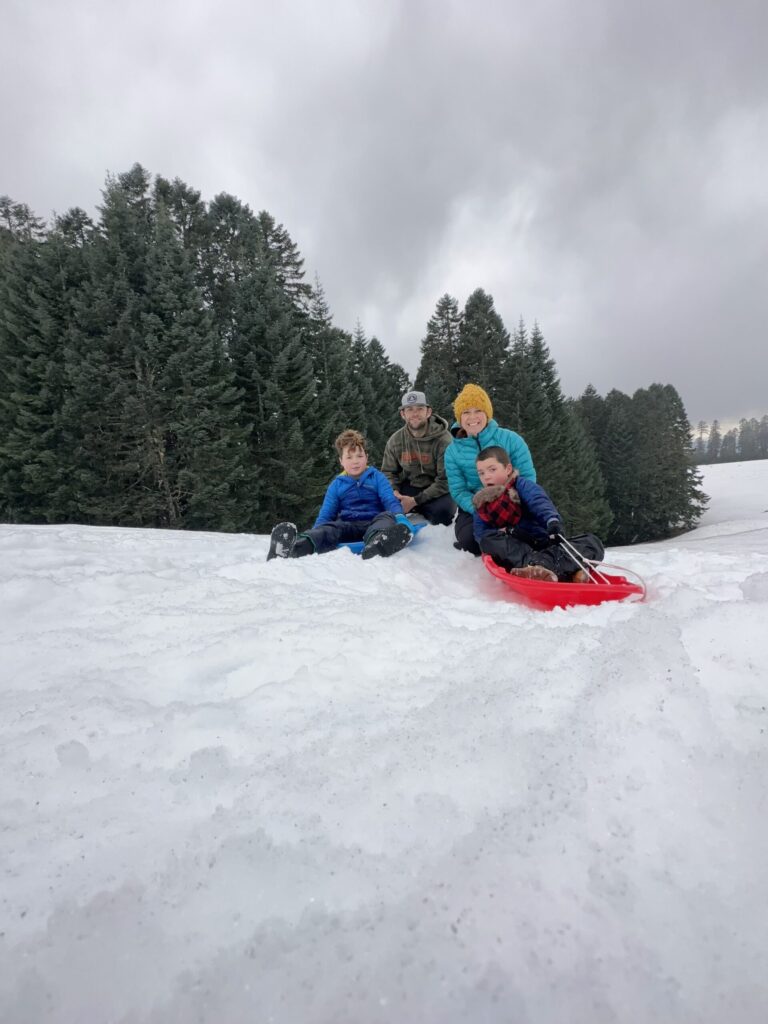 everyday motherhood. Image of man, woman, and two boys sledding in snow.
