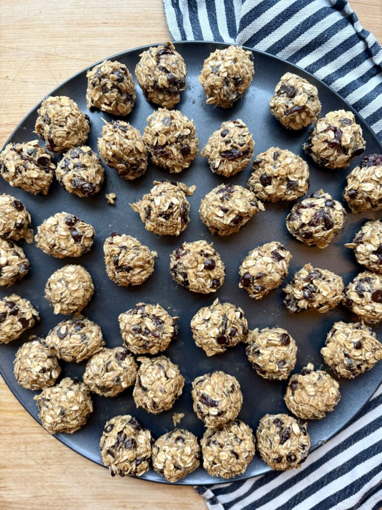 Image of oatmeal protein balls on circular sheet pan on wooden countertop and black and white cloth napkin. 