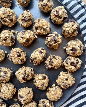 Image of no-bake peanut butter oatmeal energy balls on black circular sheet pan on black and white striped cloth napkin.