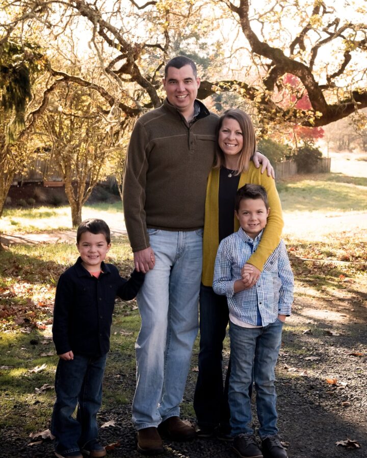 everyday motherhood. Image of family - father, mother, and two sons in Fall outfits outside under tree.