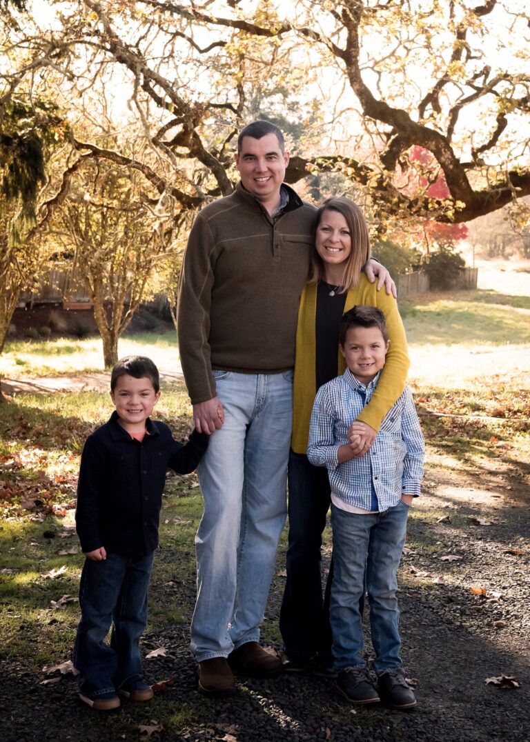 everyday motherhood. Image of family - father, mother, and two sons in Fall outfits outside under tree.